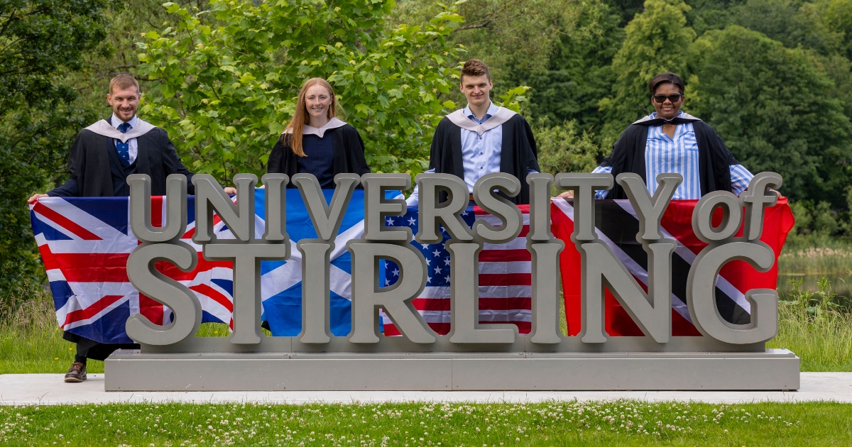 Graduating athletes pose at University of Stirling signage.