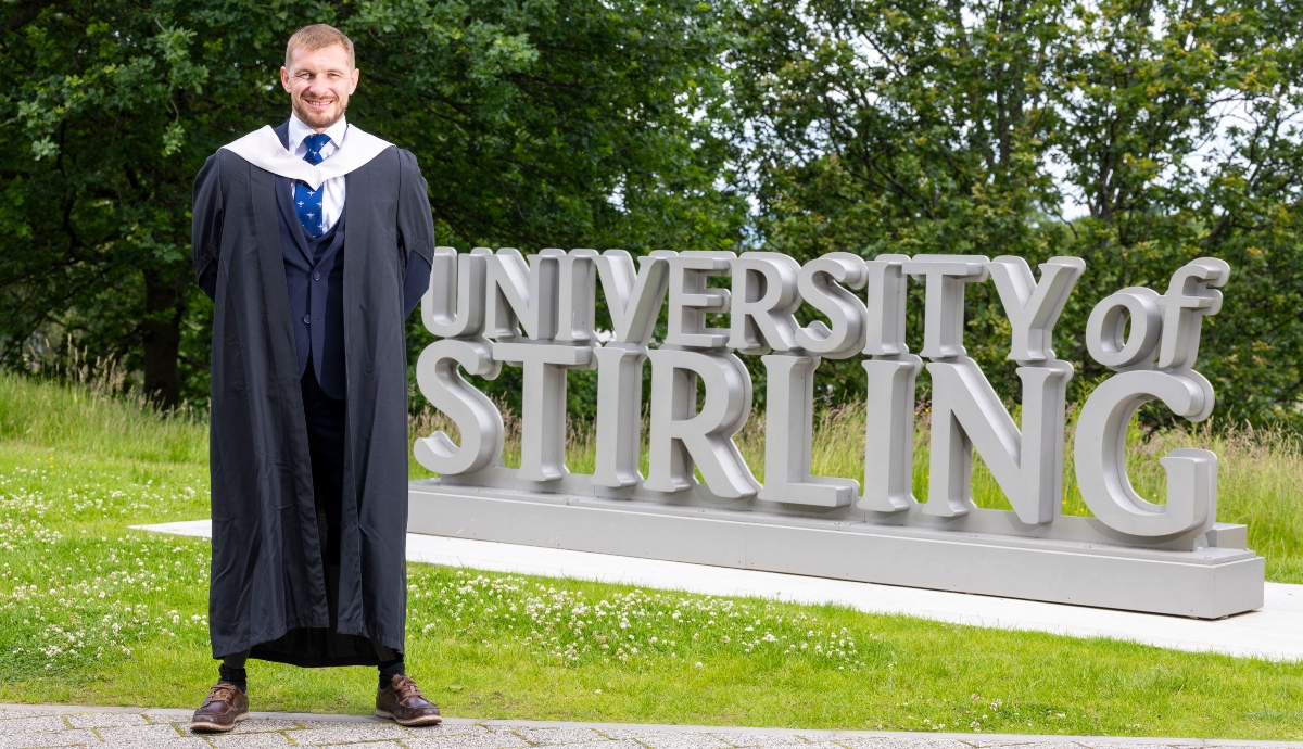 Scott Meenagh stands at the University of Stirling sign.