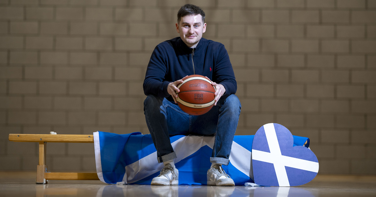 Ross sitting on a bench in a gym and holding a basketball