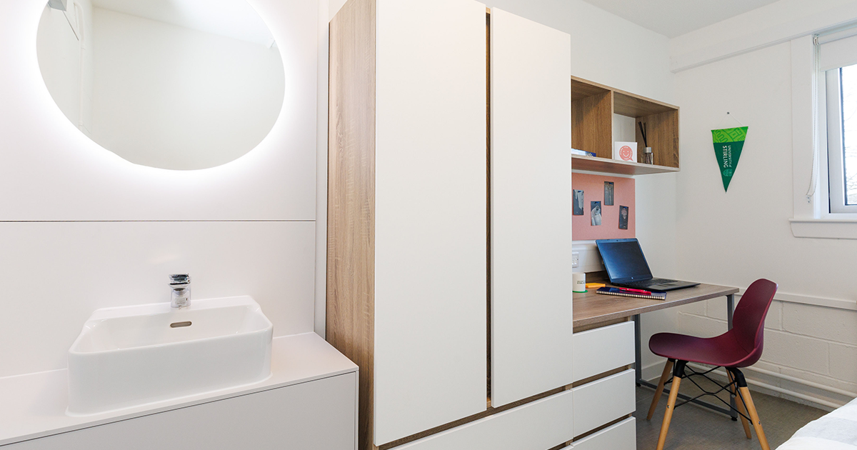 Photo of a bedroom in a student accommodation block, showing bed, sink and desk